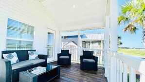 A covered porch with a dark wooden floor, white railings, and outdoor furniture including a sofa and chairs. - Vacation Cottage North Myrtle Beach #67 (North Myrtle Beach)