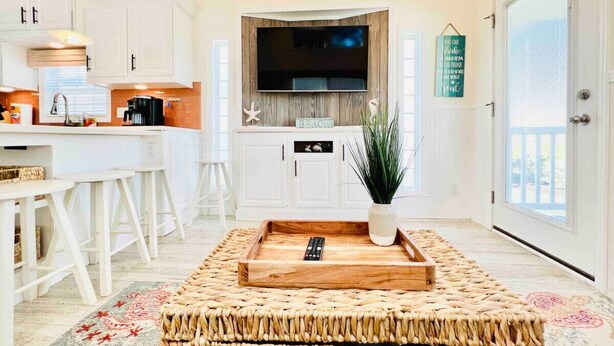 A modern kitchen with white cabinets, a large TV, and a central island with a plant. - Vacation Cottage North Myrtle Beach #67 (North Myrtle Beach)