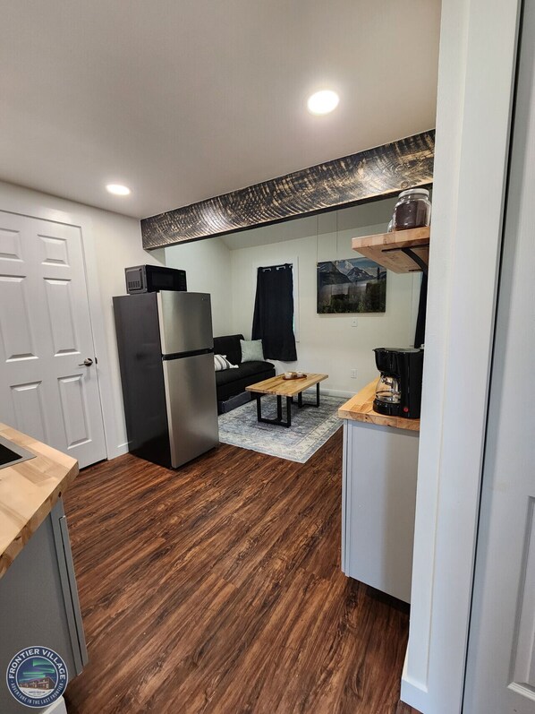 A compact kitchen with a refrigerator, microwave, and coffee maker. - The Wandering Wolf - Frontier Village (North Pole)