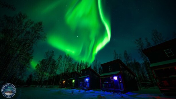 A house with a visible front porch and a snow-covered ground, under a night sky with green aurora lights. - The Wandering Wolf - Frontier Village (North Pole)