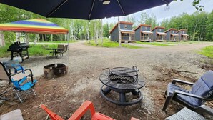 An outdoor patio area with a fire pit, outdoor furniture, and a covered seating area. - The Wandering Wolf - Frontier Village (North Pole)