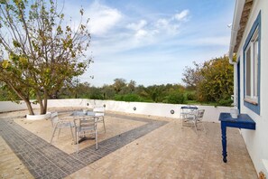 Une terrasse extérieure avec une table et des chaises, un arbre et une vue sur le paysage environnant.