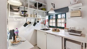 Eine Küche mit weißen Schränken, einem Spülbecken, einem Fenster mit Vorhängen und einem Vintage-Radio.