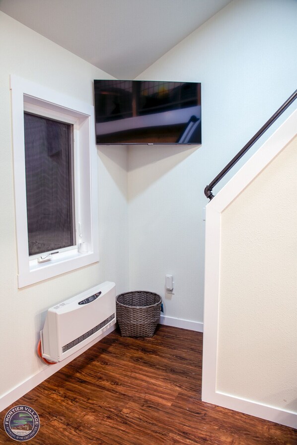 A small room with a window, a wall-mounted TV, a white heater, and a wicker basket.