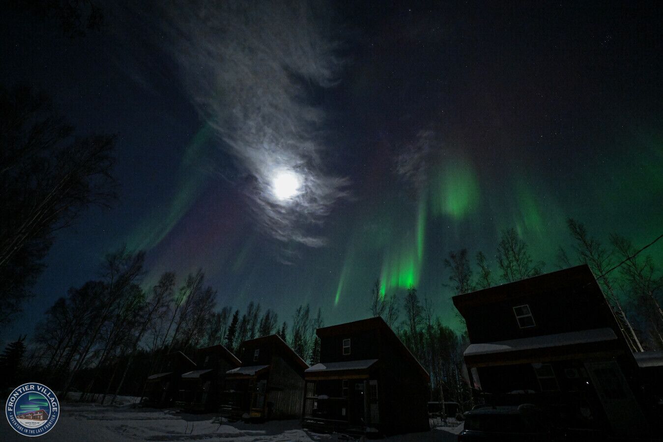 Un paisaje nevado con casas y una luna visible.