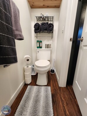 Une petite salle de bain comprenant des toilettes, un porte-serviettes, un support à papier toilette et une petite étagère avec des articles de toilette.