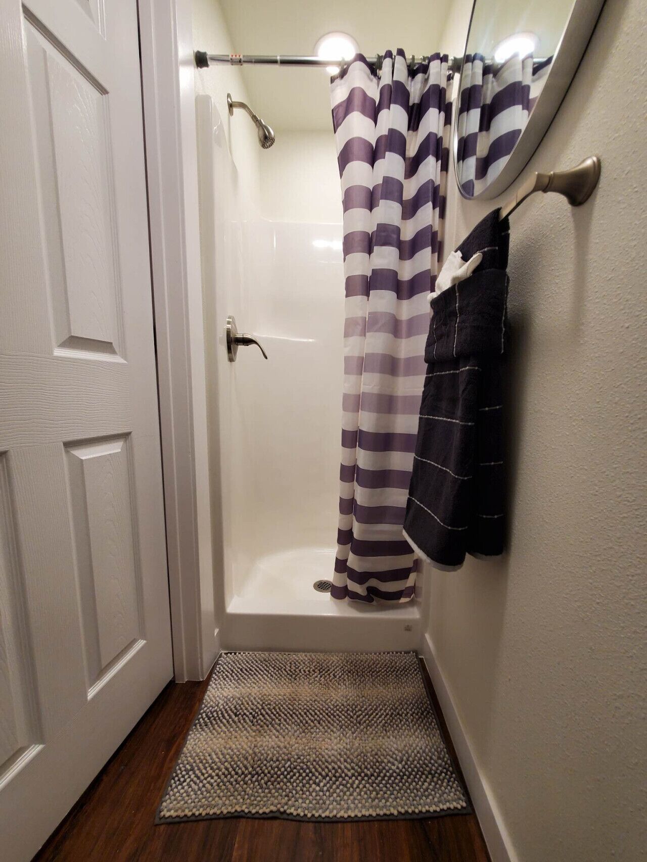 Un espace douche avec une porte blanche, un rideau de douche et un porte-serviettes.