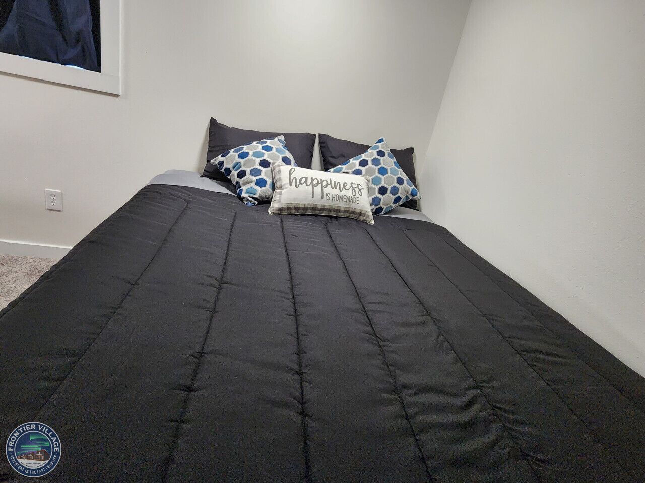 Una cama bien hecha con un edredón negro y dos almohadas decorativas.
