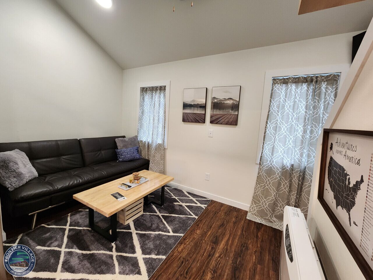 A living room with a black leather sofa, a wooden coffee table, and a patterned rug. There are two framed pictures on the wall and a map of the United States.