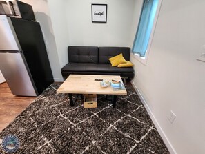 A compact living space with a kitchenette, a sofa, a coffee table, and a patterned rug.