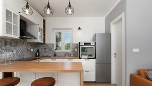 A modern kitchen with a central island, white cabinets, a built-in oven, and a stainless steel refrigerator.