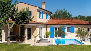 A two-story house with a swimming pool, stone pillars, and blue shutters.