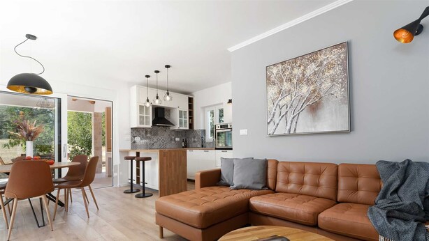 A modern living room with a brown leather sofa, a round coffee table, and a dining area with a glass table and chairs.