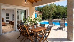 An outdoor dining area with a wooden table and chairs, a pool, and a stone wall.