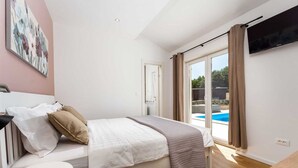 A bedroom with a bed, a TV, a painting, and a view of an outdoor swimming pool.