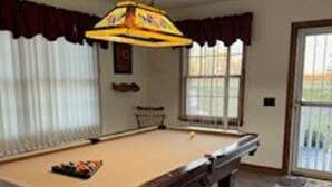 A pool table in a room with a large window, curtains, and a ceiling light fixture. - Cozy Cottage with Pool Table! (Rocky Mount)