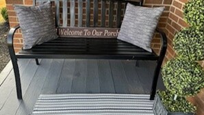A black metal bench with two grey cushions, placed on a wooden deck with a grey striped rug in front. - Cozy Cottage with Pool Table! (Rocky Mount)