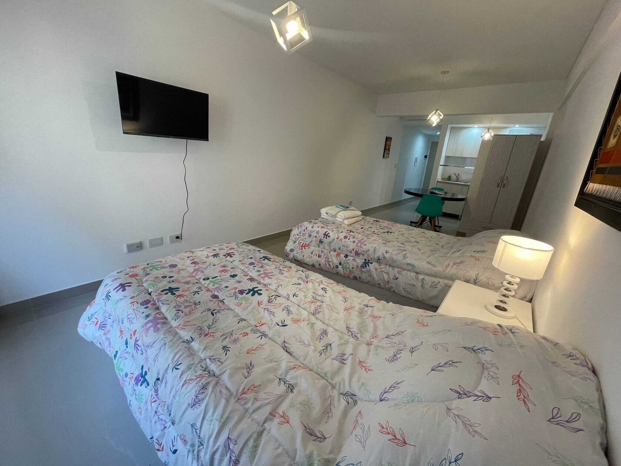 A hotel room with two beds, a flat-screen TV mounted on the wall, a desk with a chair, and a mirror reflecting the room.