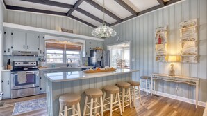 Une cuisine dotée d’un îlot central, de tabourets de bar, d’un plancher en bois et d’un luminaire suspendu.