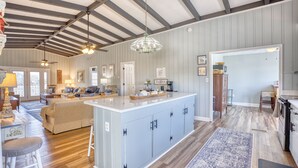 Une cuisine spacieuse dotée d’un grand îlot central, de planchers en bois et d’un plafond avec des poutres apparentes.