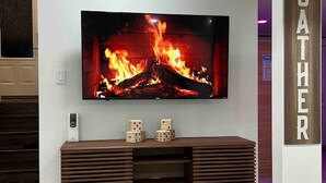 Un salon moderne avec un grand téléviseur à écran plat fixé au mur, un meuble de rangement en bois en dessous, et une pancarte sur laquelle on peut lire « RASSEMBLEMENT ».
