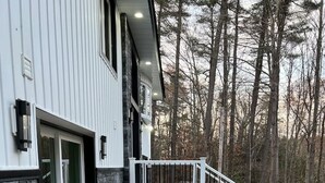 Une maison moderne dotée d’une terrasse en bois, d’une façade en pierre et d’un escalier menant à un balcon.