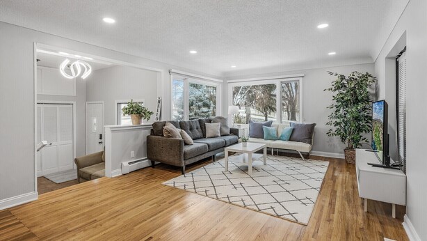 Een moderne woonkamer met een grijze bank, een witte salontafel en een groot raam met uitzicht op bomen.