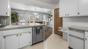 Een moderne keuken met witte kasten, een inbouw vaatwasser en een eethoek met uitzicht.