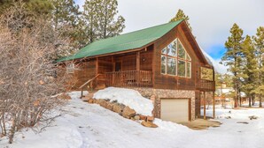 A wooden cabin with a green roof, a stone foundation, and a garage. - Pet Friendly TreeHaven Retreat (Pagosa Springs)