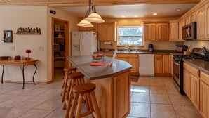 A kitchen with wooden cabinets, a central island with stools, a refrigerator, a stove, and a window providing natural light. - Pet Friendly TreeHaven Retreat (Pagosa Springs)