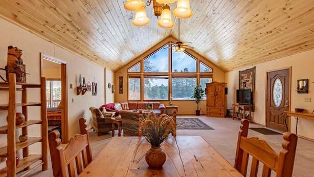 A cozy cabin interior with a wooden dining table, a sofa set, and a large window offering a view of the outdoors. - Pet Friendly TreeHaven Retreat (Pagosa Springs)