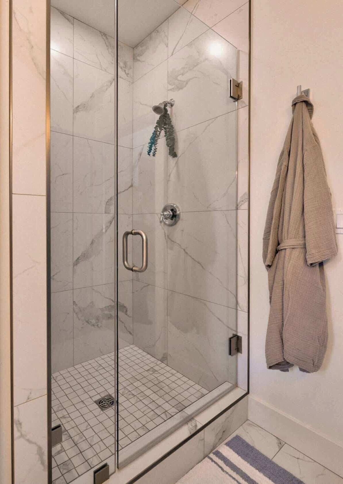 A glass-enclosed shower with a marble floor, a towel rack with a towel, and a small step leading into the shower.