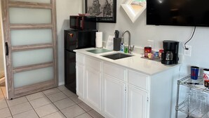 A compact kitchen with a white countertop, a black refrigerator, a microwave, a sink, and a coffee maker. There is a sliding door with frosted glass panels and a mounted television above the counter. - Easy Rider Cabin -Boat/Trailer prkg, Pet ok w/fee (Medicine Park)