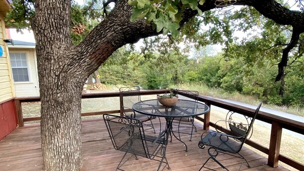 A wooden deck with a metal table and chairs, surrounded by trees. - Easy Rider Cabin -Boat/Trailer prkg, Pet ok w/fee (Medicine Park)