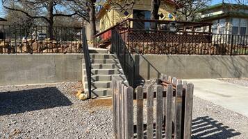 A building with a staircase leading to a porch, surrounded by a fence and trees.