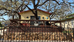 A yellow building with a red roof, surrounded by a wooden fence and a large tree. - Easy Rider Cabin -Boat/Trailer prkg, Pet ok w/fee (Medicine Park)