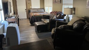 Una sala compacta con cama, sofá de cuero, escritorio y televisor.
