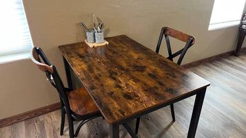 A rectangular wooden dining table with metal legs, accompanied by two chairs with wooden seats and metal frames. A small metal tray with utensils is placed on the table.