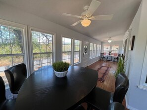 Un comedor con una mesa grande, sillas, ventiladores de techo y ventanas amplias.