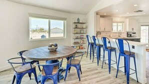 Zona pranzo con tavolo rotondo e sedie blu, cucina con mobili bianchi e vista esterna.