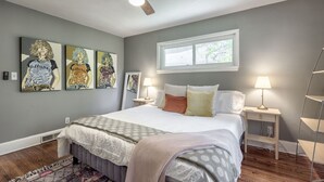 A bedroom with a bed, two bedside tables, a ceiling fan, a window, and three wall art pieces. - Caught in the City-Walk to BoPlex Coliseum and Ovens Auditorium (Charlotte)