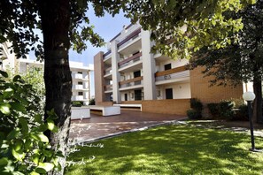A multi-story building with a flat roof, surrounded by trees and a grassy area.