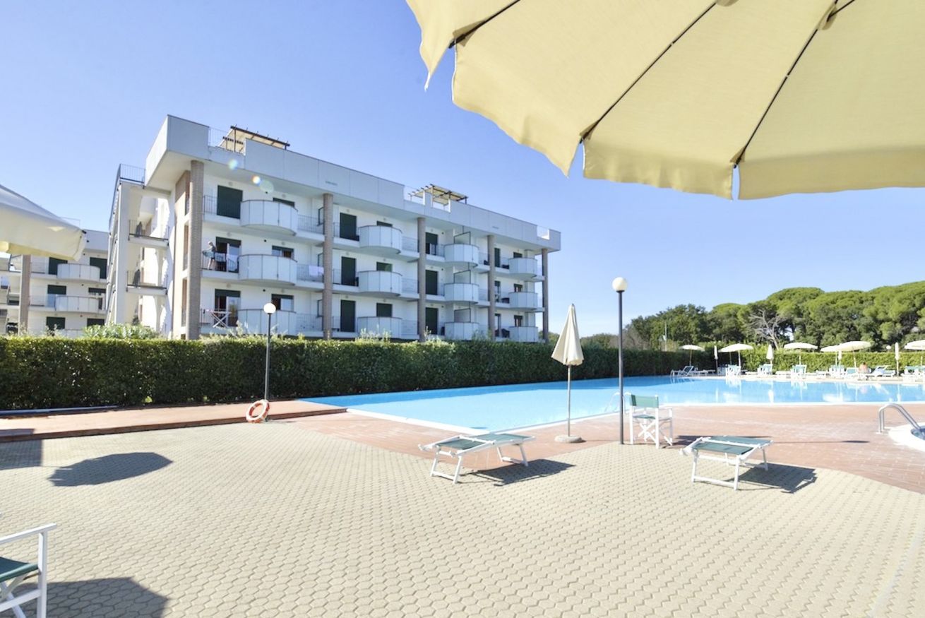 Un bâtiment moderne doté de nombreux balcons et d’un espace piscine comprenant des chaises longues et des parasols.