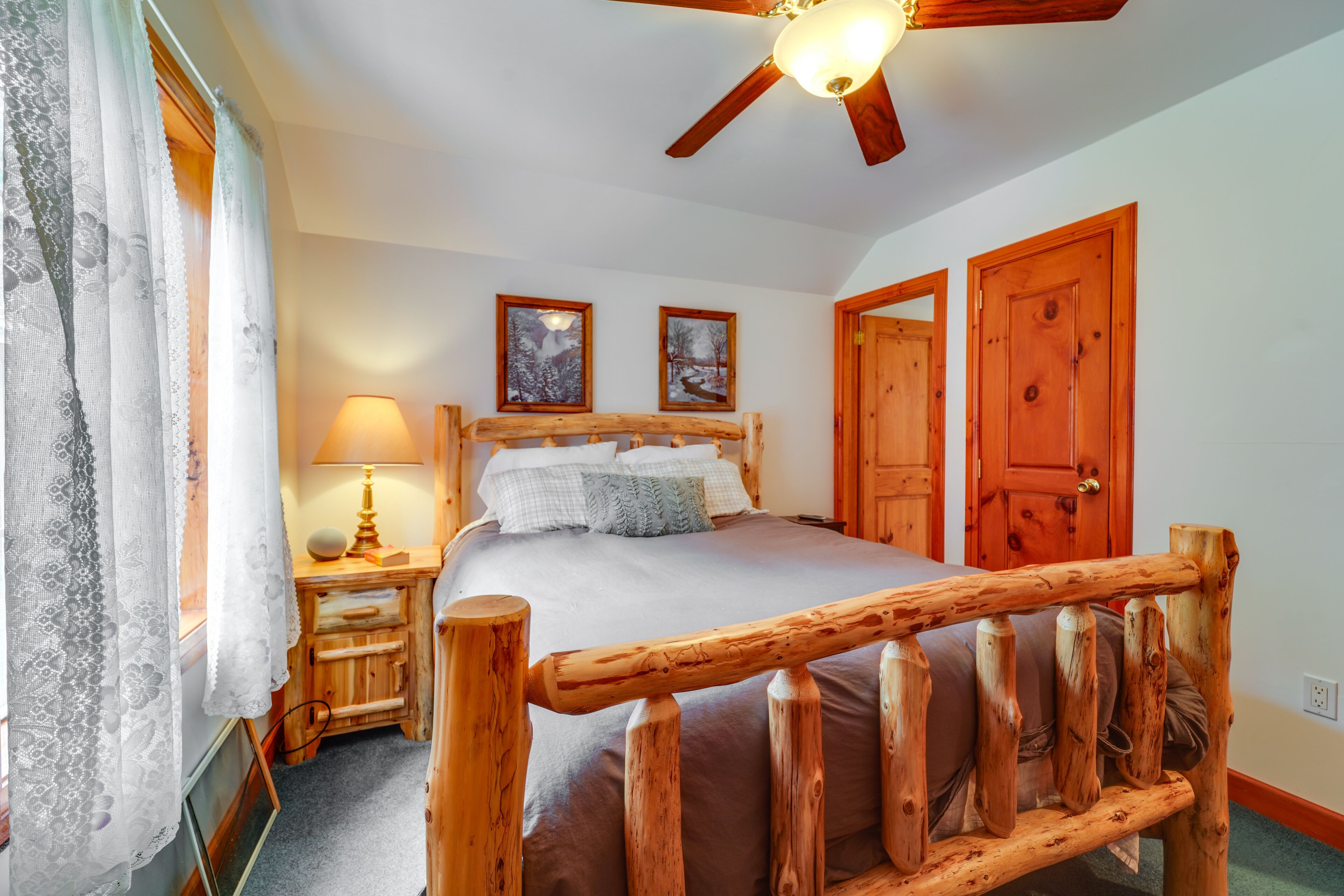 Une chambre à coucher avec un lit en bois, un ventilateur de plafond, une lampe de chevet et deux tableaux encadrés accrochés au mur.