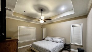 Un dormitorio con cama, ventilador de techo y dos ventanas con persianas.