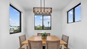 A dining area with a wooden table and four chairs, a hanging light fixture, and large windows offering a view of the cityscape. - Rooftop Ocean-View Home, Private Parking, Near Beach (Oceanside)