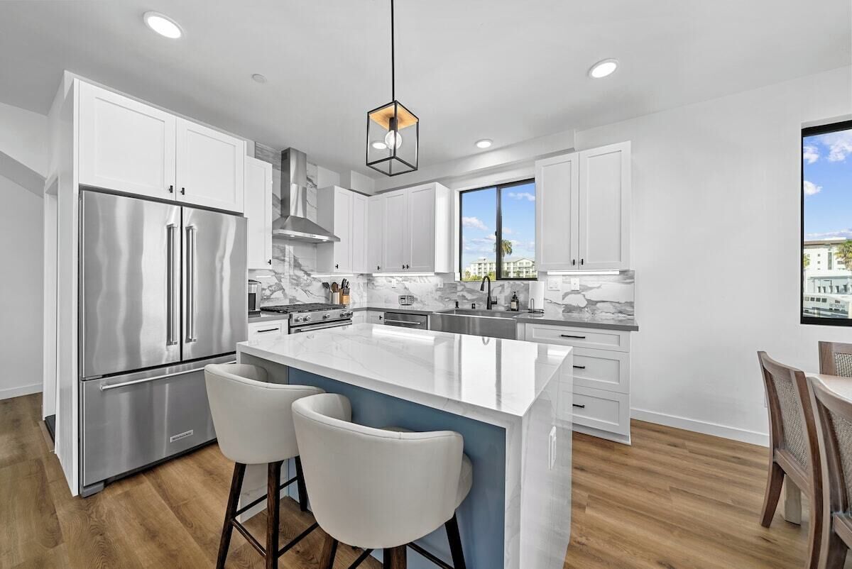 A modern kitchen with white cabinets, stainless steel appliances, a marble countertop, and a large island with bar stools.