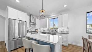 A modern kitchen with white cabinets, stainless steel appliances, a marble countertop, and a large island with bar stools. - Rooftop Ocean-View Home, Private Parking, Near Beach (Oceanside)