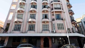 Um edifício de vários andares com varandas, uma entrada central e uma placa com um logotipo.