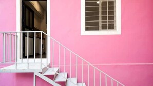 Um edifício rosa com uma escadaria branca e uma janela com padrão de grade.